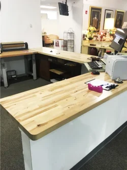 Retail checkout counter with wood surfaces, computer, printer, papers, and office supplies in a well-lit store space.