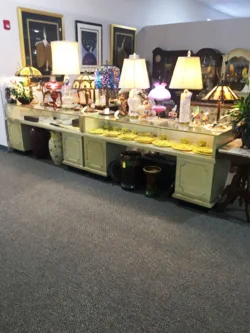 A long vintage console table displays antiques, lamps, and decorative items against a wall in a carpeted room.