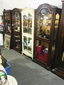 Four wooden display cabinets, one painted white, filled with various collectibles in an antique store setting.