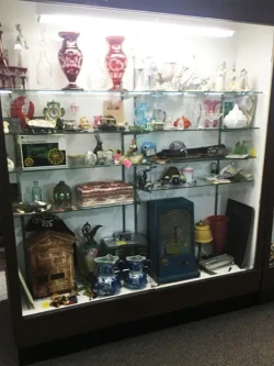 Glass display case filled with assorted vintage items, including ceramics, vases, figurines, and an old radio.