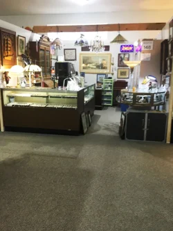 Antique shop interior with glass display cases, vintage lamps, framed art, and collectibles on shelves and walls.
